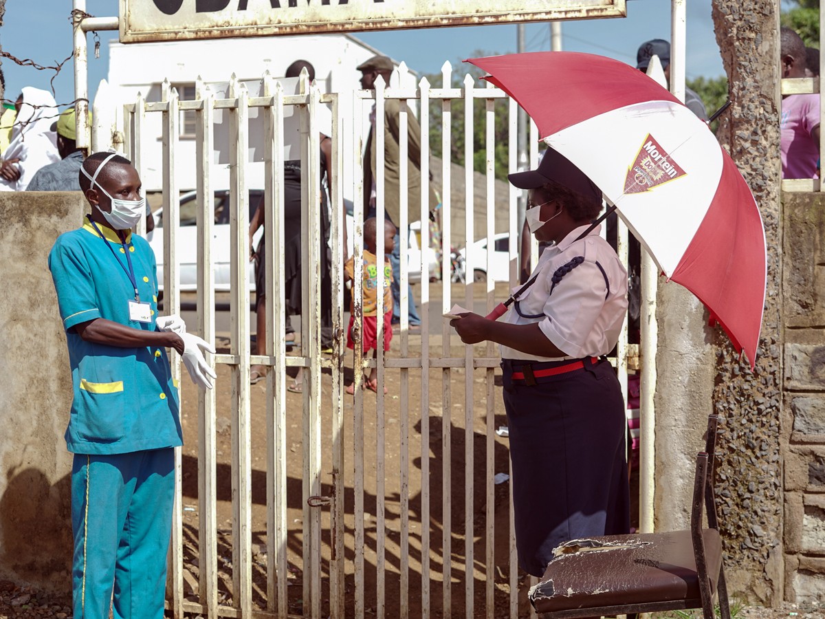 Health worker and security guard in PPE standing at a gate at a clinic in Kenya