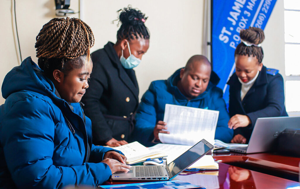Four people in uniforms and coats look at papers and a computer on a conference table.